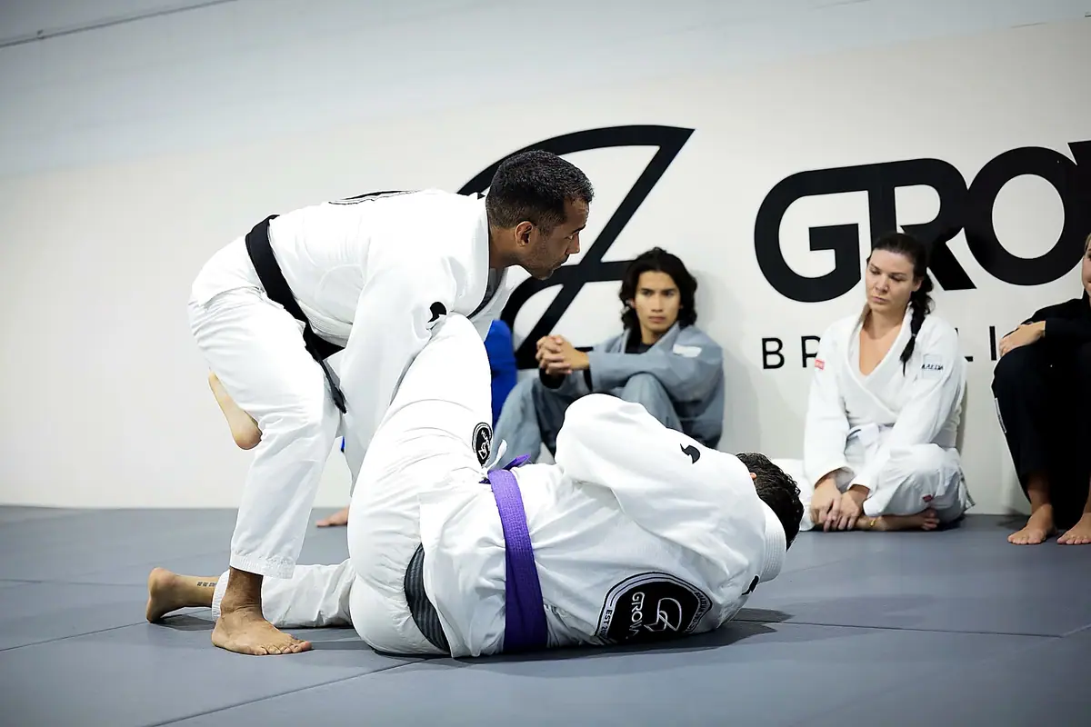 Ícaro coaching a purple belt while students watch from the wall
