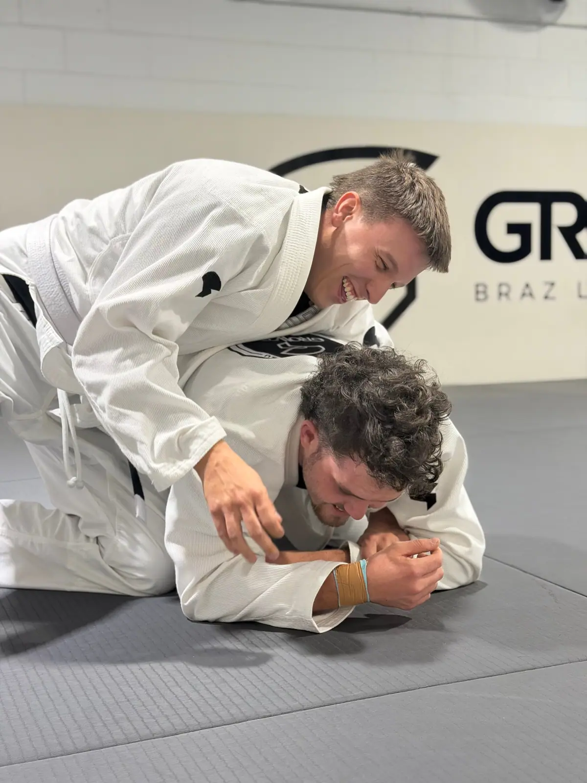 Two students smiling while rolling in the gi