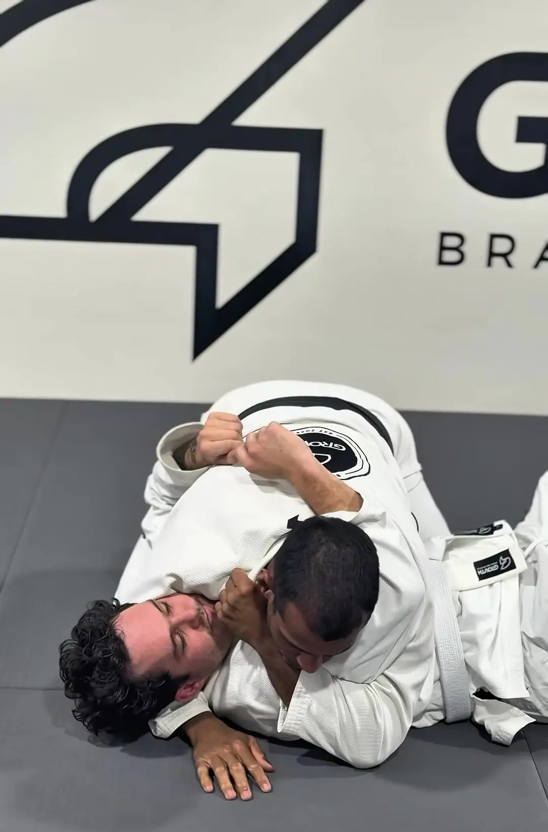 Ícaro demonstrating a technique from side control in front of the Growth logo